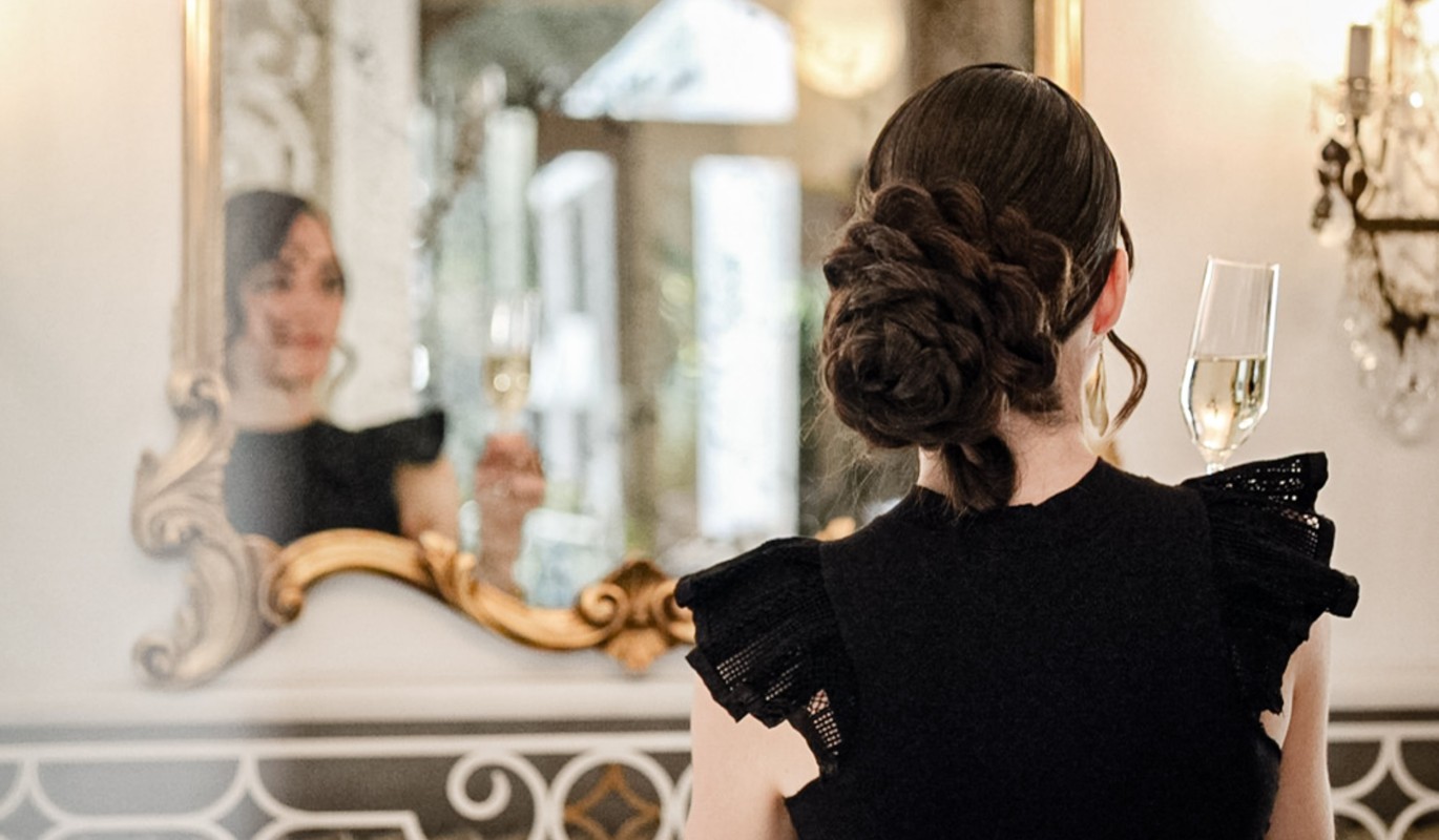 Frau vor Spiegel mit Sektglass im Stadthotel Meranerhof in Meran Südtirol